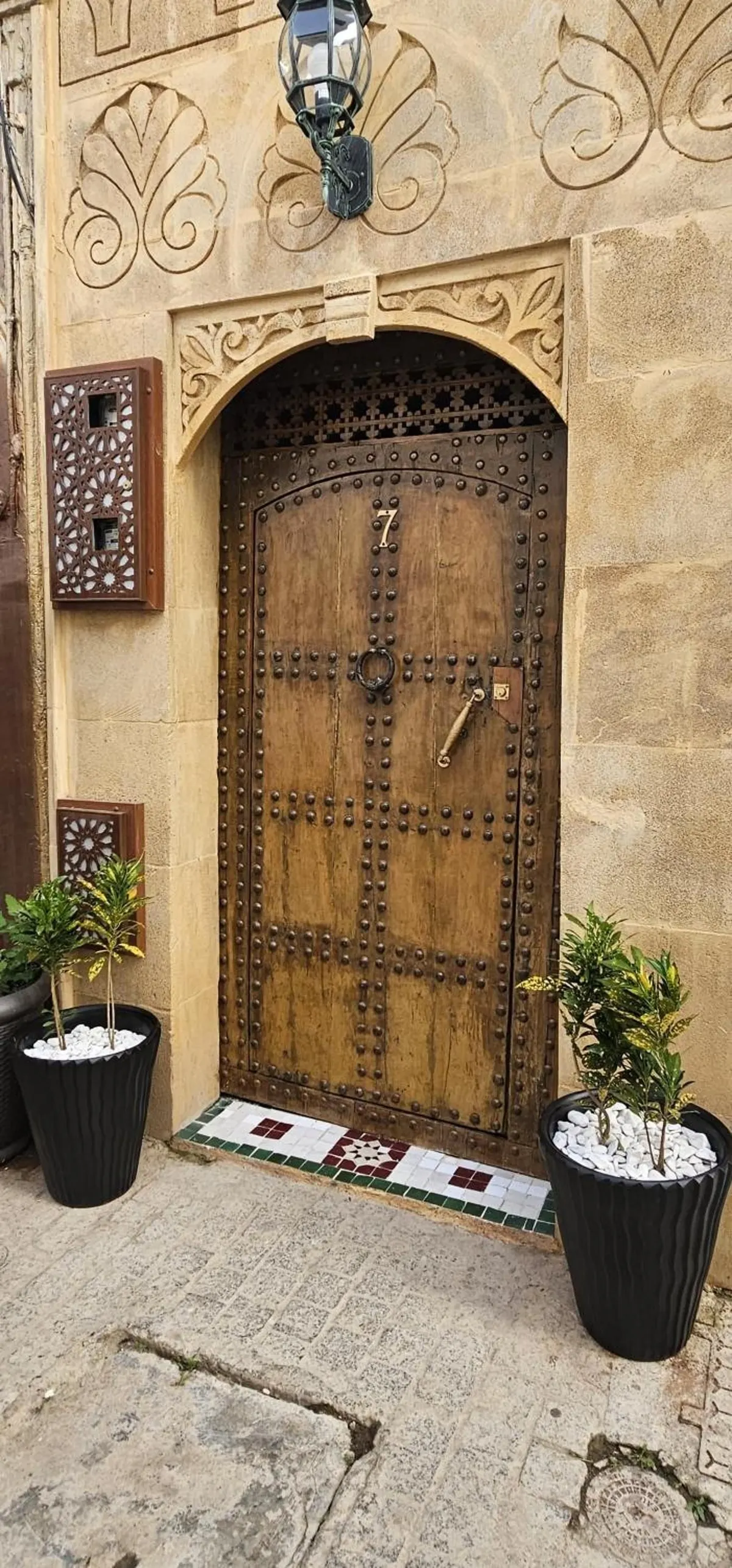 Façade du n° 7 : porte cloutée en bois sous un arc de pierre sculptée, lanterne en fer forgé au-dessus, arbustes en pot
