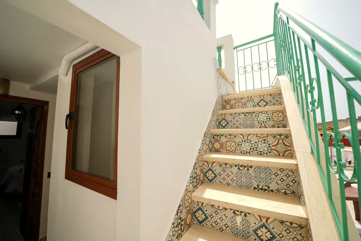 Patterned tile risers and a green iron rail, climbing past the rooms.