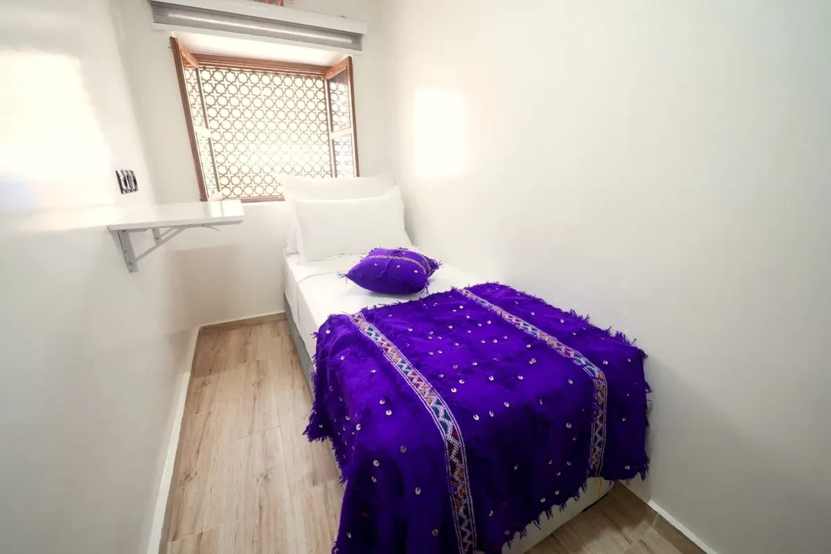 Single room with a violet handira blanket and a carved window grille