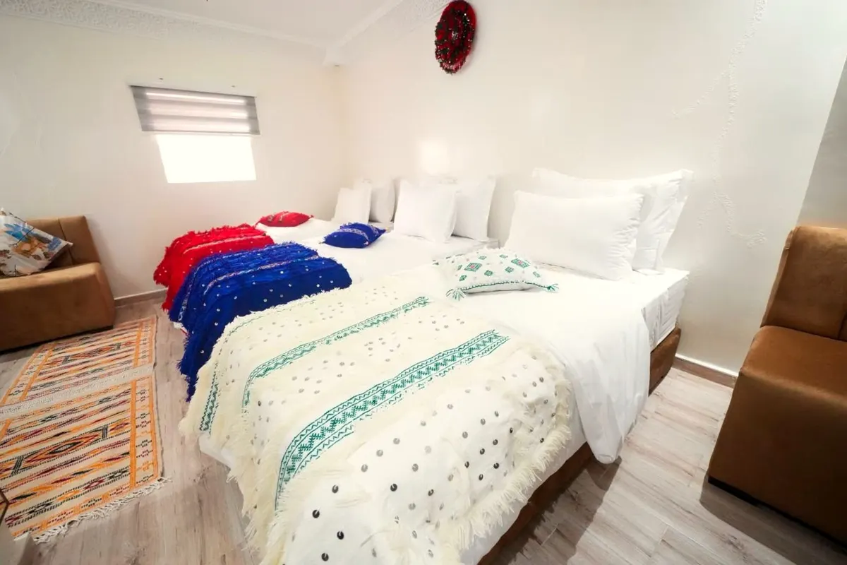 Triple room: a double and a single bed with cream handira blankets, tan sofas and a kilim