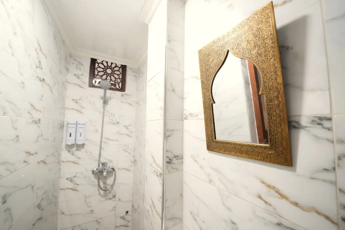 Triple shower room: marble-effect tiles, walk-in shower and a carved brass mirror