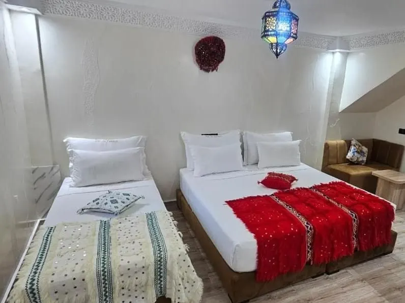 A double bed with a red handira blanket beside a single bed, blue glass lantern