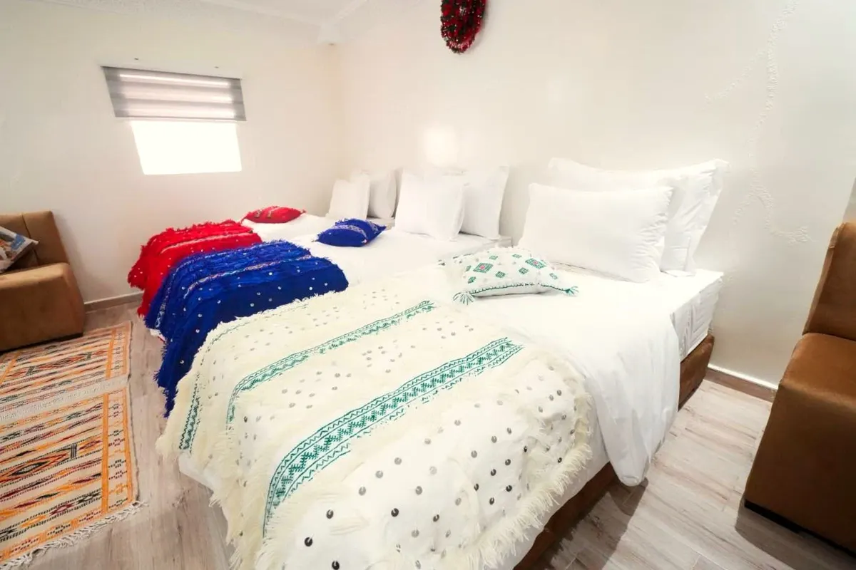Triple room: a double and a single bed with cream handira blankets, tan sofas and a kilim