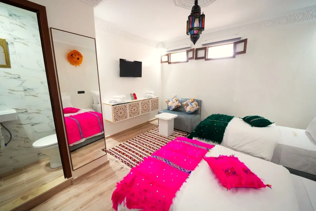 Twin room: two single beds, a fuchsia handira blanket, a stained-glass lantern and the shower-room door open