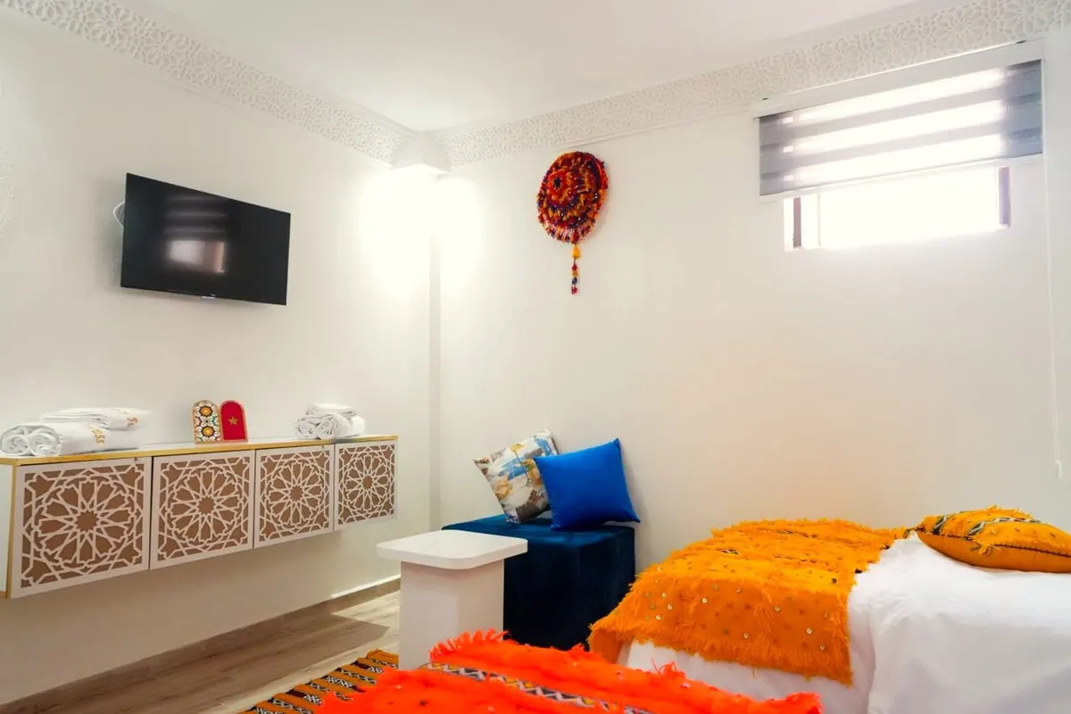 Orange handira blanket, cobalt ottoman and a red woollen pompom on the white wall